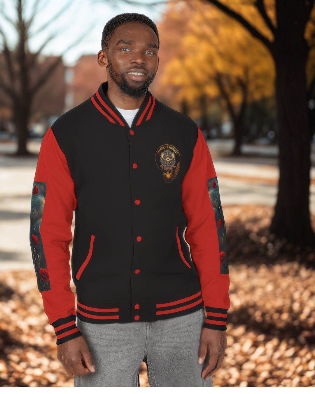 Man wearing a black and red varsity jacket in an outdoor setting with trees and fallen leaves.